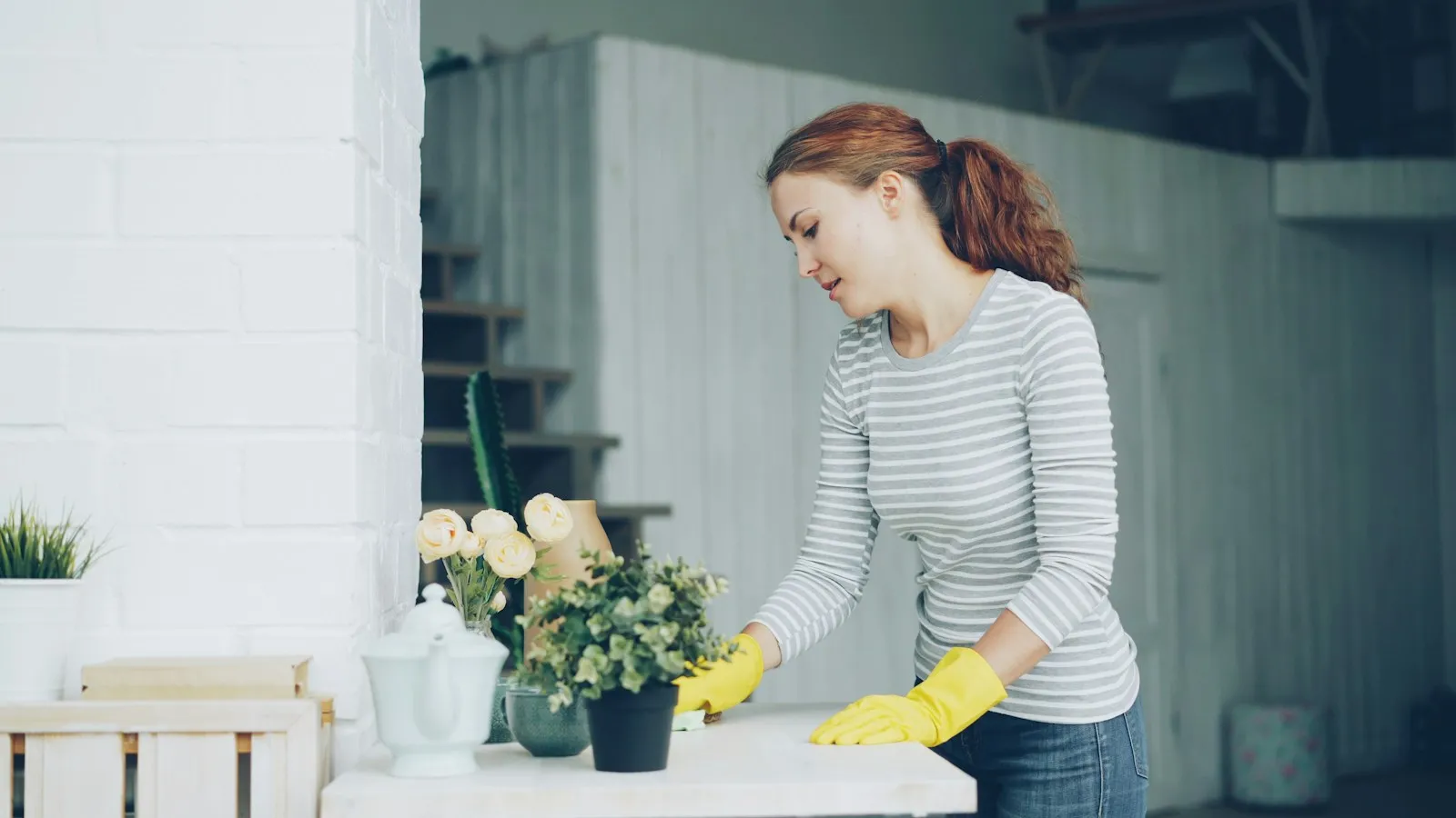 Woman in yellow rubber gloves wiping dust off a white table at home