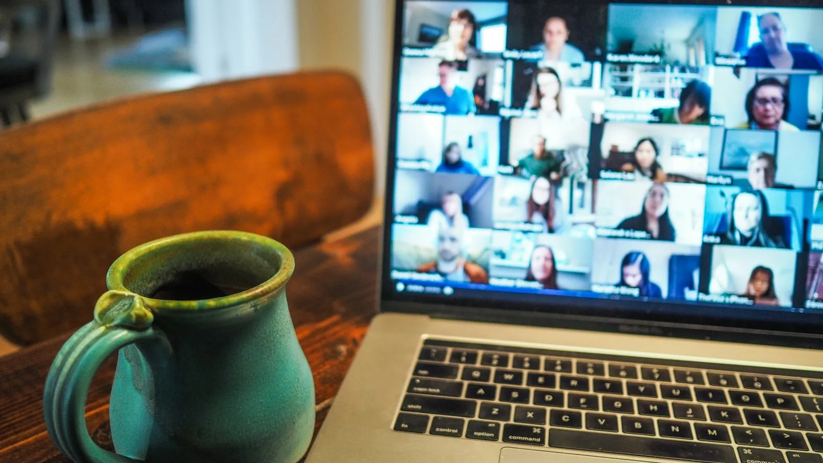 Laptop showing a video call grid next to a coffee mug