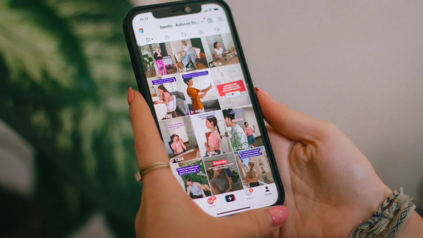 Hand holding a phone with a folder of social media apps open in front of a leafy plant