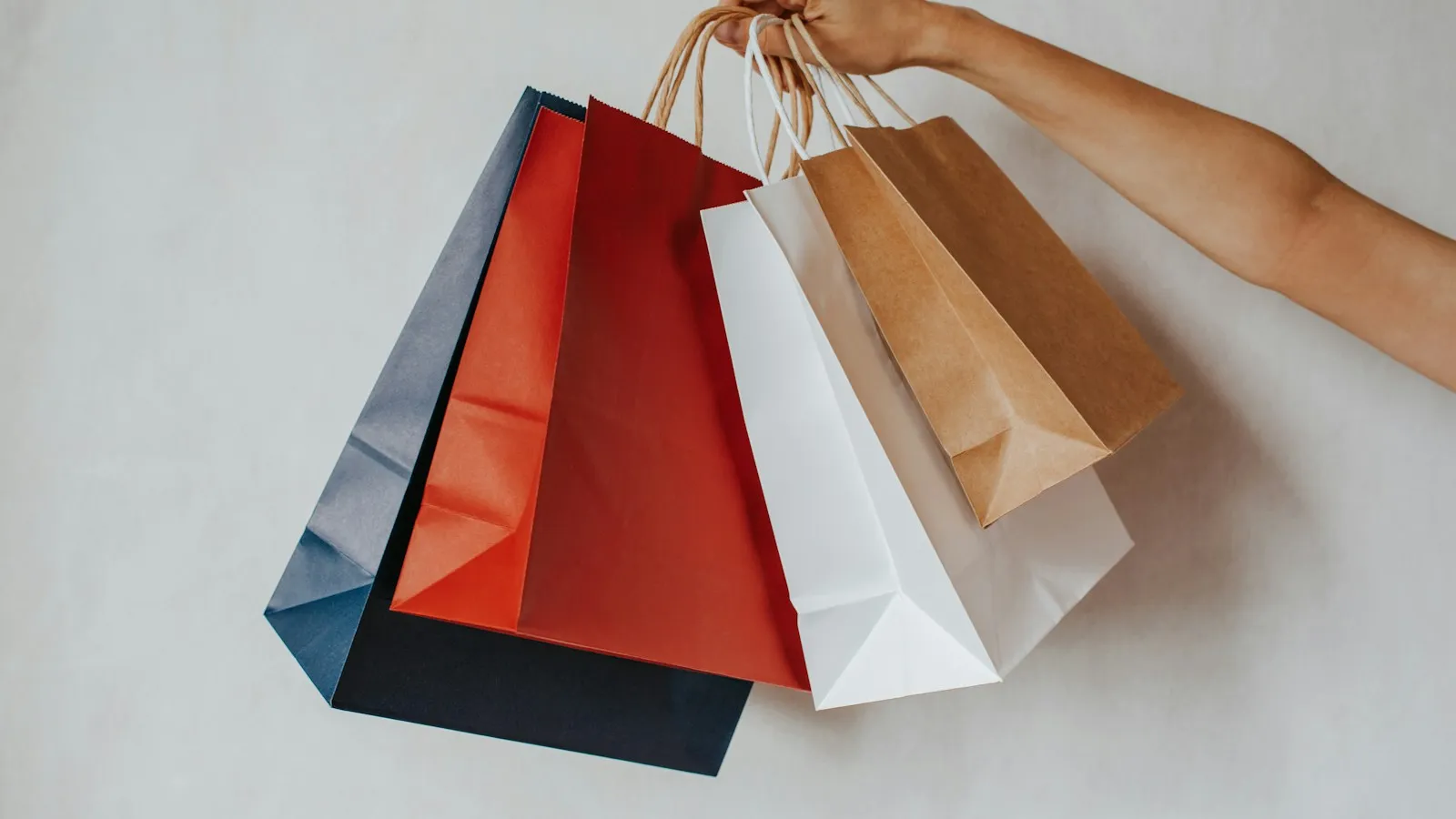Hand holding several colorful paper shopping bags