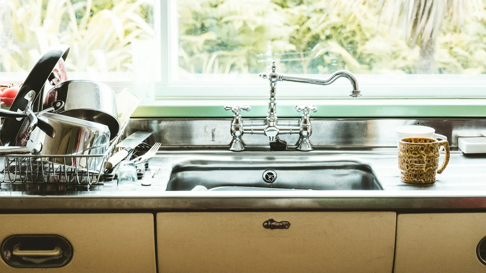 A stainless steel kitchen sink with a vintage faucet under a bright window